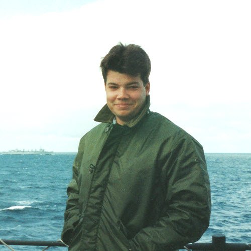 man standing near water with a military boat in the water